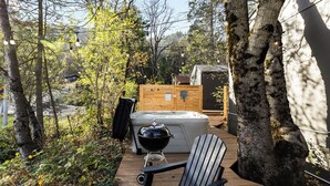 A wooden deck with a hot tub, a grill, and a chair. - Modern Cabin (Alder) (Dunsmuir)