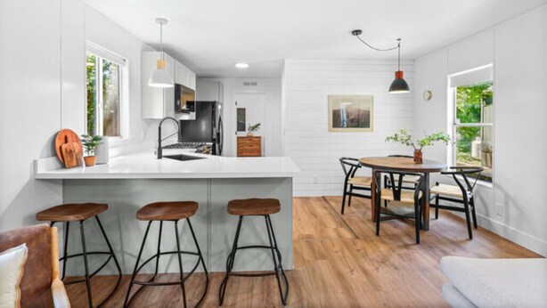 A modern kitchen with a central island, bar stools, and a dining area with a table and chairs. - Modern Cabin (Alder) (Dunsmuir)