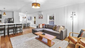 Een moderne woonkamer met een grijze modulaire bank, een houten salontafel, en een eethoek met een witte tafel en stoelen.