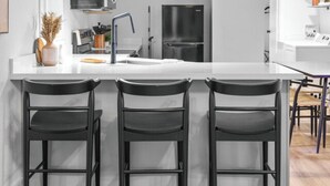 Een moderne keuken met een wit kookeiland, zwarte barkrukken, een zwarte koelkast en een roestvrijstalen spoelbak.