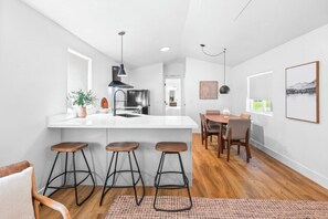 A modern kitchen with a white countertop, bar stools, and a dining area with a table and chairs.