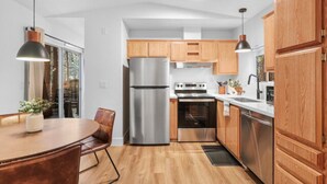 Une cuisine moderne dotée d’appareils électroménagers en acier inoxydable, de meubles en bois et d’un coin repas avec une table et des chaises.