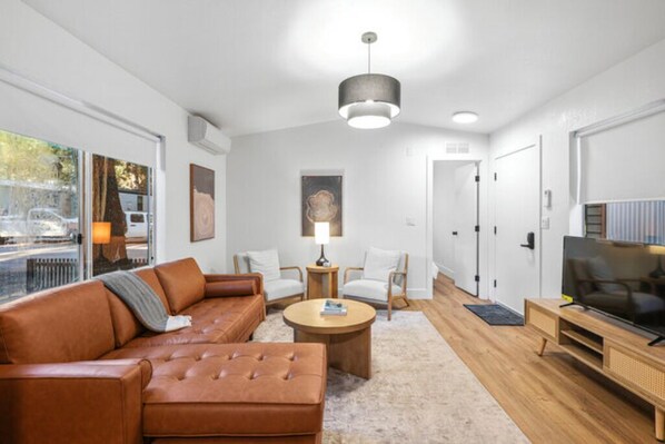 Een moderne woonkamer met een bruine leren bank, een ronde salontafel en een tv-meubel.