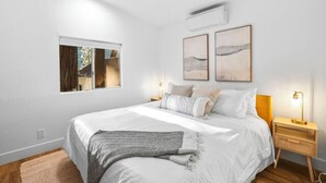 Une chambre à coucher avec un grand lit, deux tables de chevet, une fenêtre et des œuvres d’art accrochées au mur.
