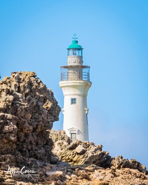 Ein Leuchtturm mit weißer Struktur und grüner Spitze, umgeben von felsigem Gelände.