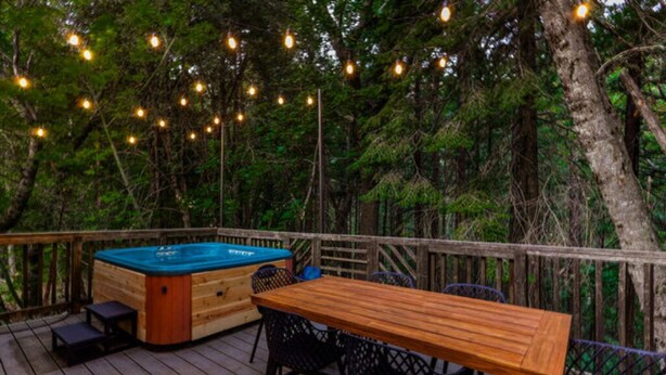 Een houten terras met een jacuzzi, een houten tafel en stoelen.