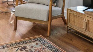 Een woonkamer met een houten stoel, een gekleurd kussen, een televisie en een kast.