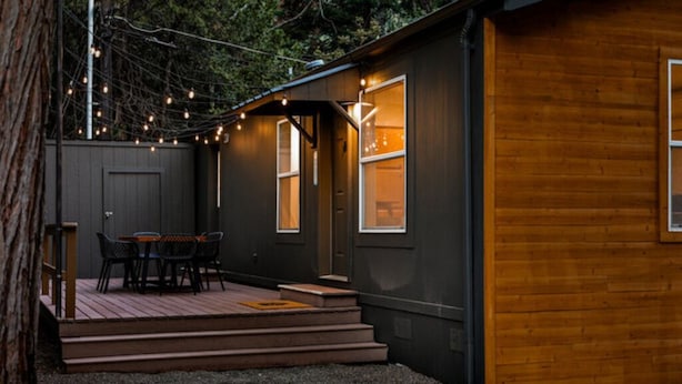 Un piccolo chalet con veranda in legno, un tavolo e sedie, e luci decorative.