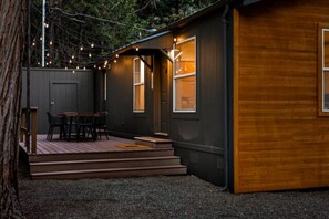 A small cabin with a wooden deck, a table and chairs, and string lights. - Modern Cabin - (Pine) (Dunsmuir)