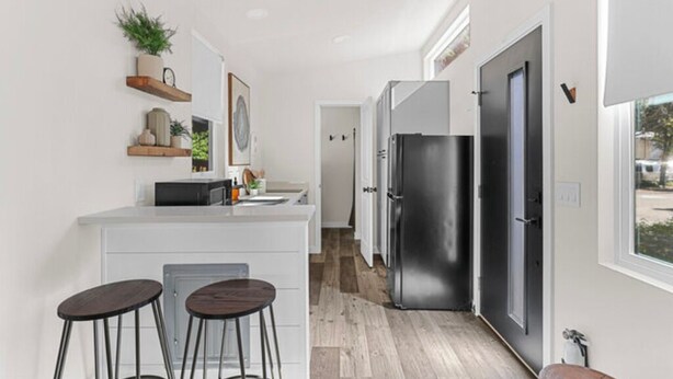 A modern kitchen with white cabinetry, a black refrigerator, and two stools. - Tiny Home  - (Beech) (Dunsmuir)
