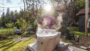 A hot tub outdoors with a wooden deck, surrounded by trees and a grill. - Tiny Home  - (Beech) (Dunsmuir)