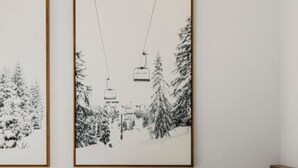 A bedroom with a bed, white bedding, and two framed pictures of a snowy landscape with a ski lift. - Tiny Home  - (Cedar) (Dunsmuir)