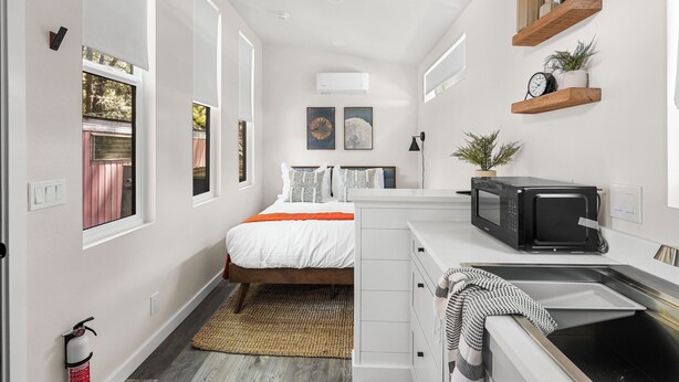 A compact, modern bedroom with a bed, bedside tables, and a small kitchenette. - Tiny Home   -  (Koa) (Dunsmuir)