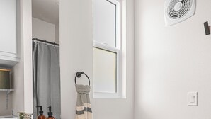 A modern bathroom with a white vanity, a toilet, a window, and a wall-mounted fan.