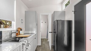 A modern kitchen with white cabinetry, a stainless steel refrigerator, and a window with an exit sign.