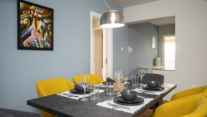 Un coin repas avec une longue table dressée pour quatre personnes, des chaises jaunes et un luminaire suspendu moderne.
