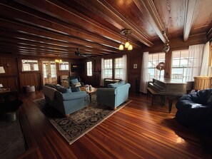 L’intérieur d’un chalet accueillant, avec un plancher en bois, un canapé, un fauteuil, un piano et une table à manger.