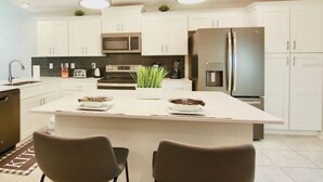 A modern kitchen with white cabinets, stainless steel appliances, and a central island with two chairs.