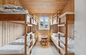 A narrow room with wooden bunk beds, a small stool, and a window with a view of a house. - Nice home in Sydals with WiFi (Sydals)