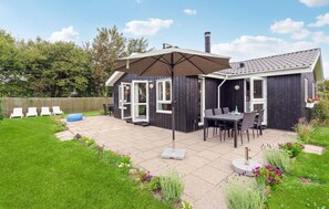 A small, dark wooden house with a patio, a table with chairs, and a large umbrella. - Nice home in Sydals with WiFi (Sydals)