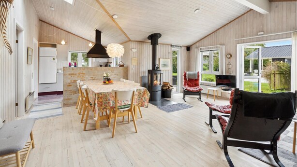 Un vaste espace de vie comprenant une grande table en bois, une cheminée et une vue sur le jardin, accessible par une porte-fenêtre coulissante.