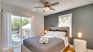 Un dormitorio con cama, ventilador de techo, mesita de noche y vistas al exterior.