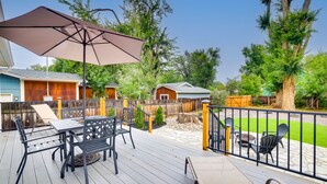 Una terraza de madera con mobiliario exterior, una pérgola y vistas a un área boscosa.