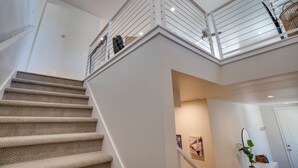 A multi-level interior with a carpeted staircase, white walls, and a ceiling with recessed lighting.