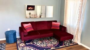Una sala de estar con sofá rojo, alfombra estampada y chimenea.