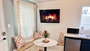 Una habitación acogedora con una zona de estar con bancos integrados, una pequeña mesa redonda, un televisor montado en la pared, un microondas y un lavavajillas.