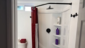 Zona de ducha con cortina roja, cabezal de ducha de mano y estantes con artículos de aseo.