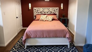 Un dormitorio con una cama blanca, un tapete estampado, una pared roja y un aire acondicionado instalado en el techo.