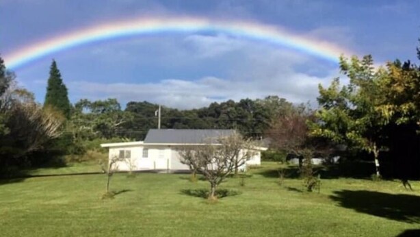 Une maison avec une pelouse et un arc-en-ciel dans le ciel.