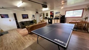 Un salon comprenant une table de ping-pong, un canapé, une table à manger avec des chaises et un coin cuisine.