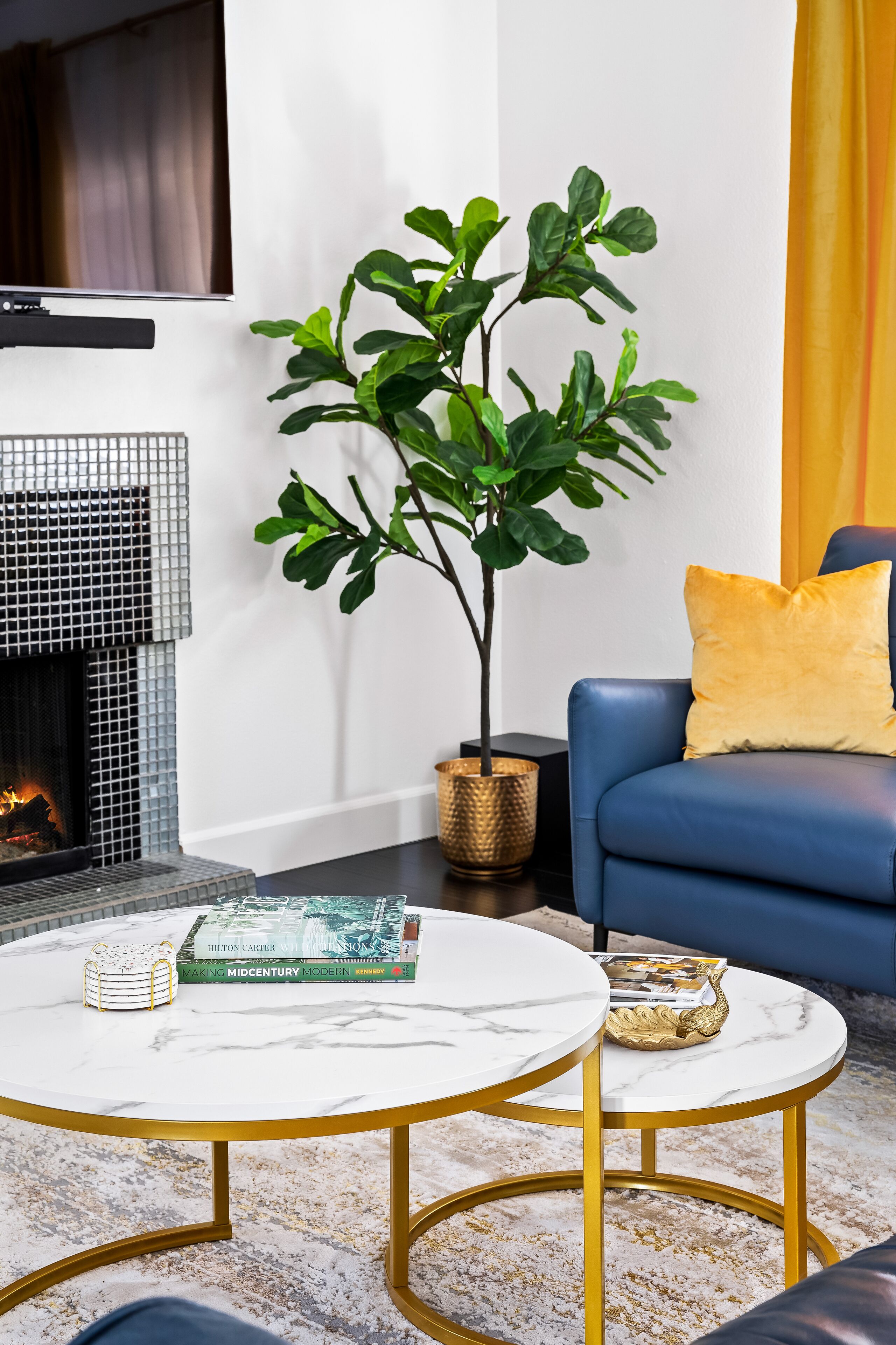Ein modernes Wohnzimmer mit Kamin, einem blauen Sofa und zwei weißen Marmortischen mit goldenen Beinen.