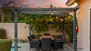 An outdoor patio with a pergola, string lights, and a table with chairs. - Paradise Springs, 4br Pool&Spa 5min to Downtown PS (Palm Springs)