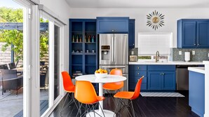 A modern kitchen with blue cabinets, a stainless steel refrigerator, and a round table with orange chairs. - Paradise Springs, 4br Pool&Spa 5min to Downtown PS (Palm Springs)