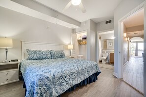 Een slaapkamer met een groot bed, nachtkastjes, een plafondventilator en uitzicht op de badkamer.
