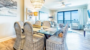 A dining area with wicker chairs and a glass table, a chandelier, and artwork on the walls.