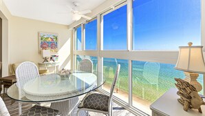Una habitación con una mesa de vidrio, sillas de mimbre, una lámpara y vista al océano.