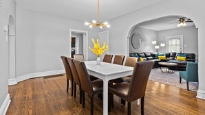 A dining area with a white table and brown chairs, a vase with yellow flowers, and a ceiling light fixture. - Botanical Bliss | JZ Vacation Rentals (St. Louis)