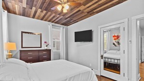A bedroom with a bed, a dresser, a TV, and a door leading to another room. - Botanical Bliss | JZ Vacation Rentals (St. Louis)