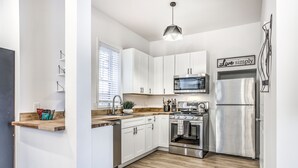 A modern kitchen with white cabinets, a stainless steel refrigerator, a microwave, and a stove. - Hidden Gem | JZ Vacation Rentals (St. Louis)