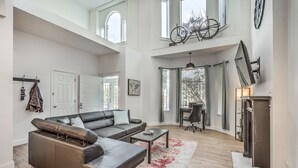 A spacious living room with a sectional sofa, a coffee table, and a fireplace. There are large windows and a high ceiling. - Hidden Gem | JZ Vacation Rentals (St. Louis)