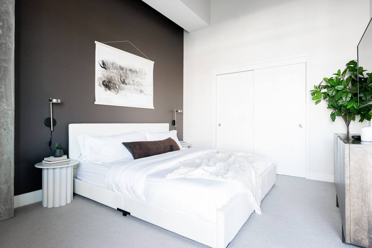 Une chambre moderne avec un lit blanc, un mur d’accent de couleur grise, une porte et une plante.