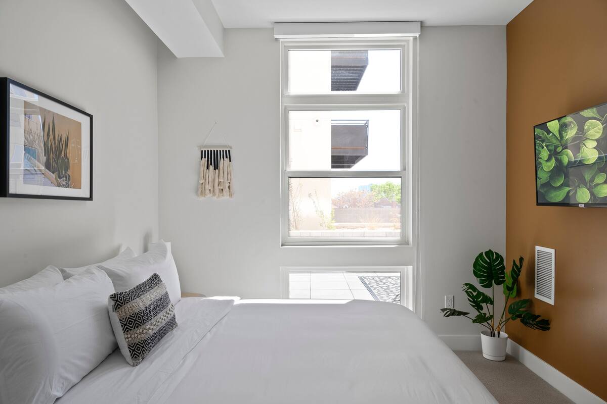 Une chambre à coucher avec un grand lit, une fenêtre, une plante et un tableau encadré au mur.