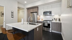 A modern kitchen with a central island, stainless steel appliances, and a dining area with two chairs. - Espadin Condos II (Denver)