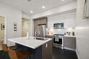 A modern kitchen with a central island, stainless steel appliances, and a dining area with two chairs. - Espadin Condos II (Denver)