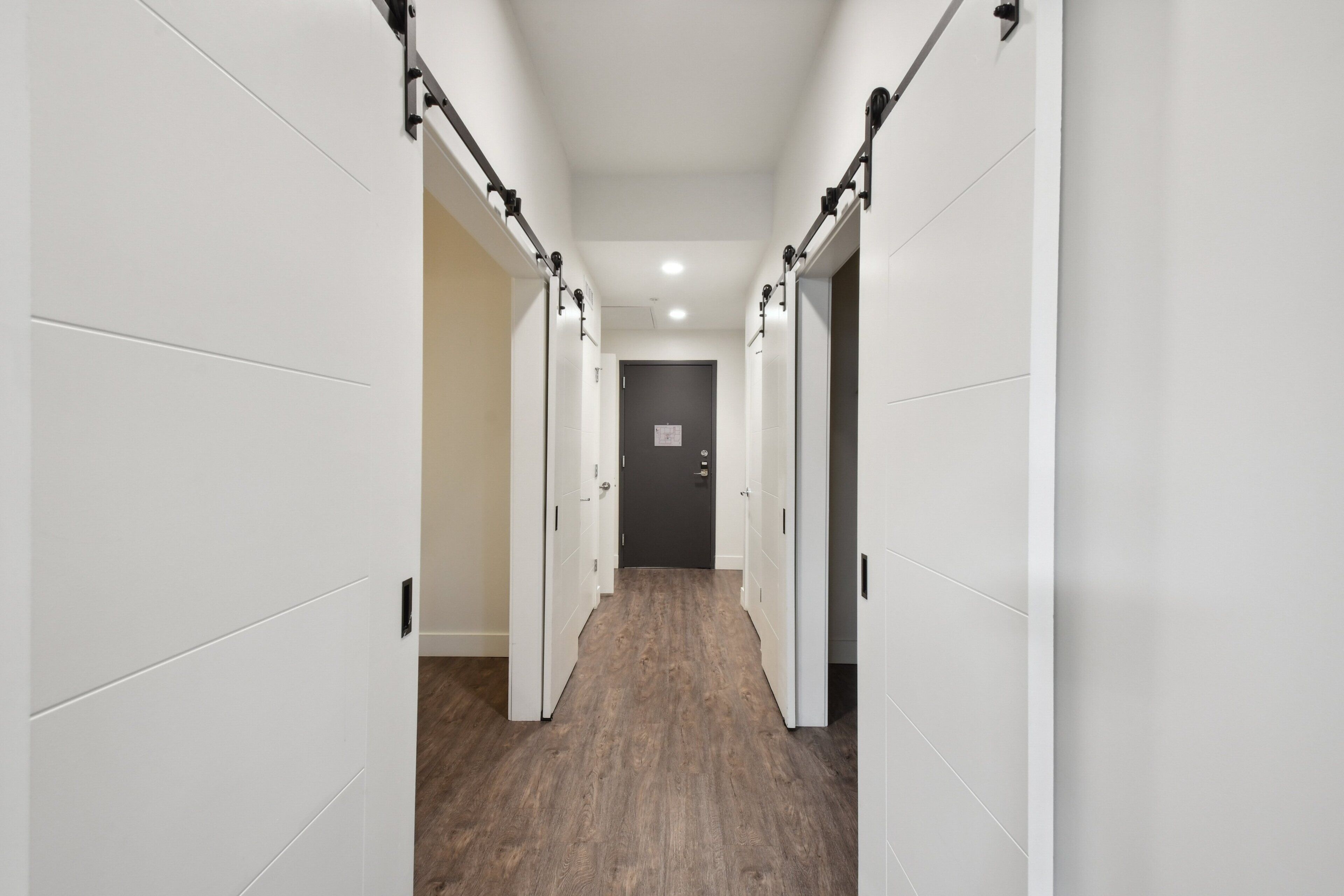 A hallway with white walls and wooden flooring, leading to a door at the end.