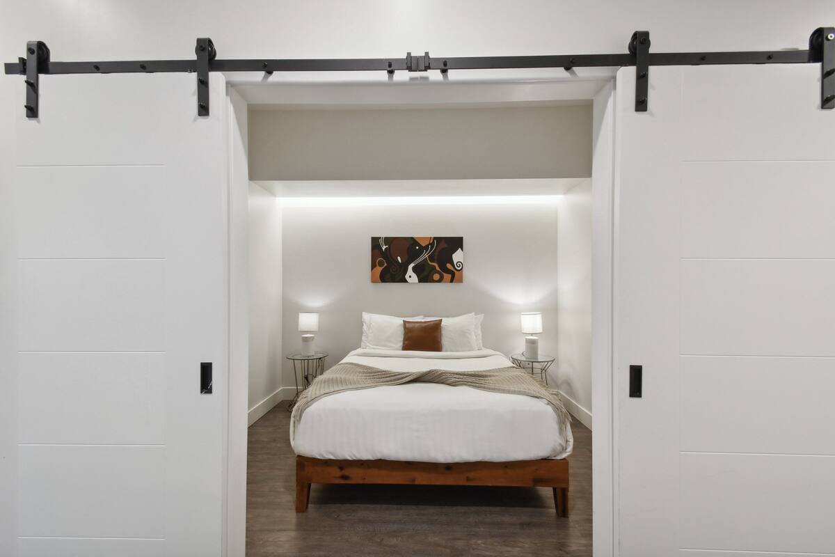 Une chambre à coucher avec un lit, des murs blancs, un plancher en bois et une porte coulissante de style grange, de couleur noire.
